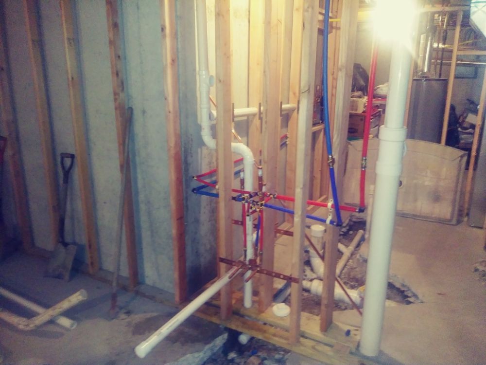 Construction site with exposed wall studs, PVC pipes, and tools in a partially finished room