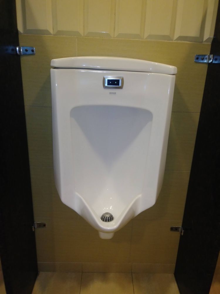 White wall-mounted urinal in a restroom stall with dark side panels and yellow tiled walls