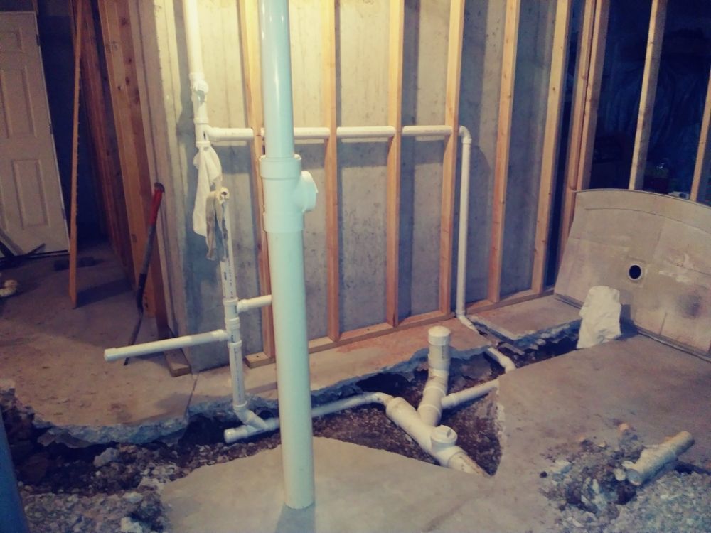 Unfinished basement framing with exposed pipes, insulation, and rough plumbing trench in the floor