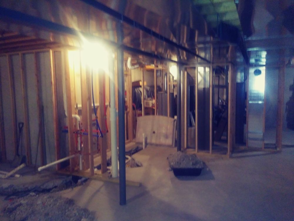 Dimly lit unfinished room with exposed wooden framing, a bright work light, and construction debris on the floor