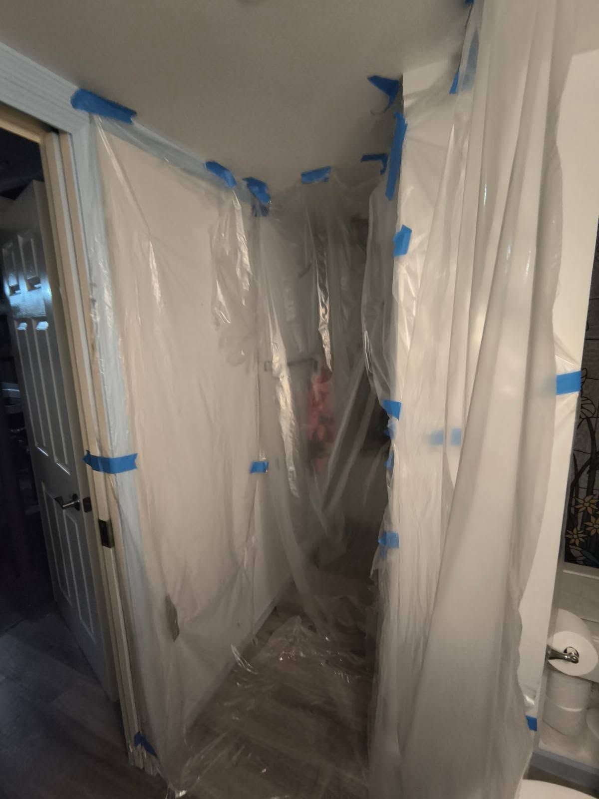 Hallway covered in clear plastic sheeting and blue painter’s tape during renovation