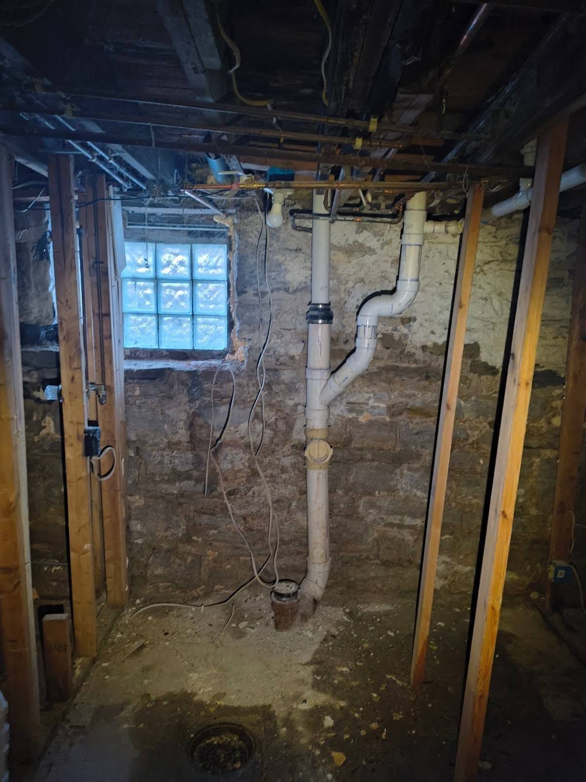 Basement crawlspace with exposed pipes, dirt floor, and a small glass-block window
