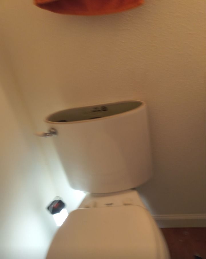 Toilet with the tank lid off, viewed close-up in a bathroom corner.