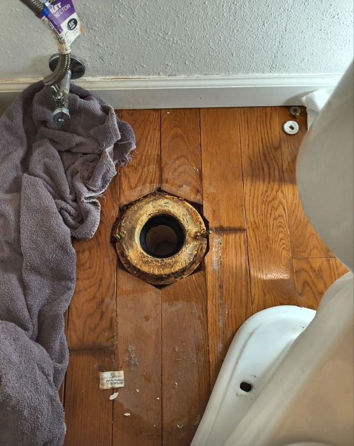 Bathroom floor with exposed toilet drain hole, towel, and toilet base visible