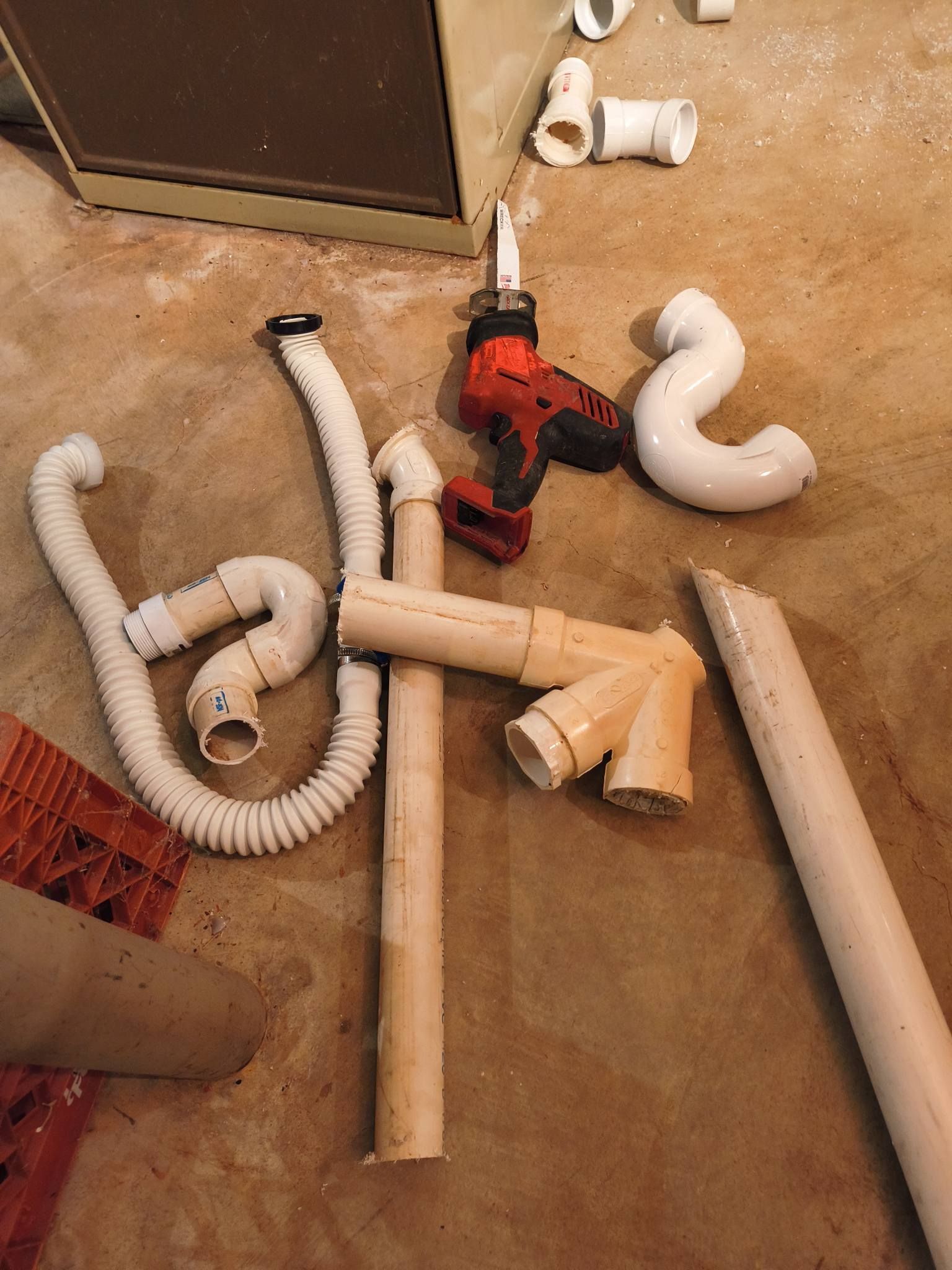 Scattered dryer vent hoses and pipes on a dusty floor beside a red drill and an appliance.