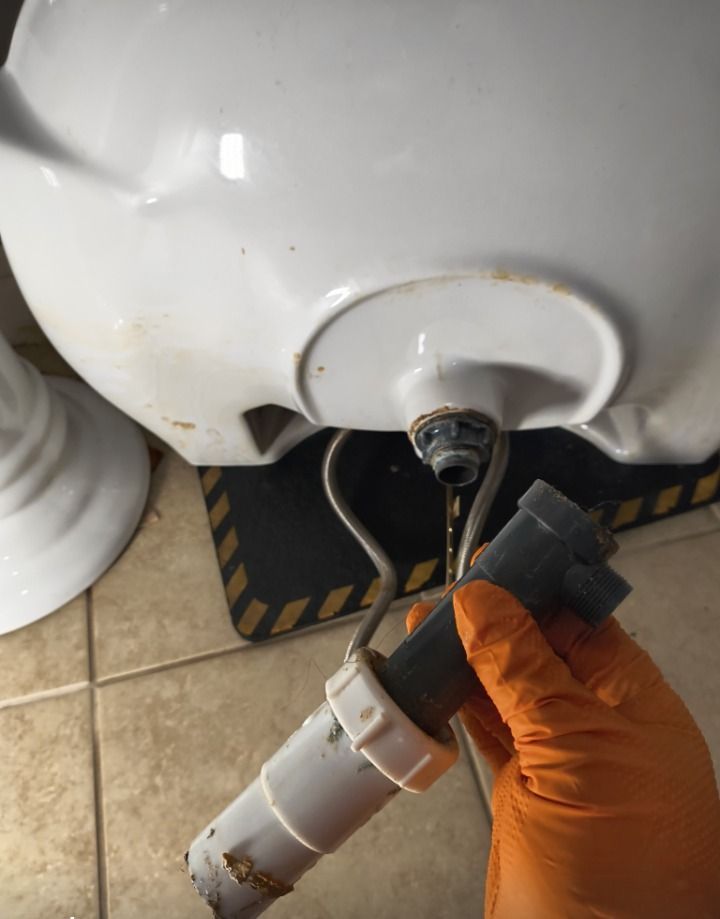 Hand holding a disconnected white hose beneath a sink drain on a tiled floor