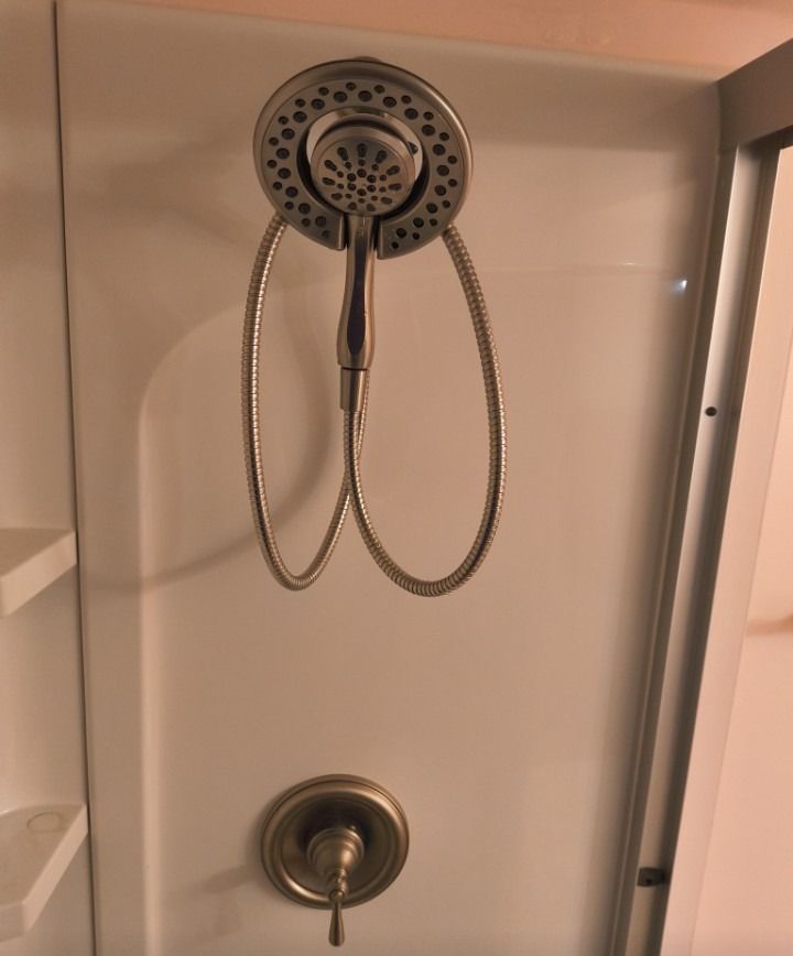 Shower stall with chrome showerhead, handheld wand, and faucet on white tile wall