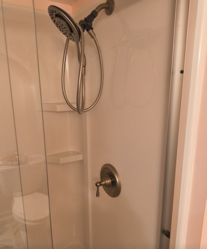 Shower stall with handheld showerhead, sliding glass door, and built-in corner shelf.