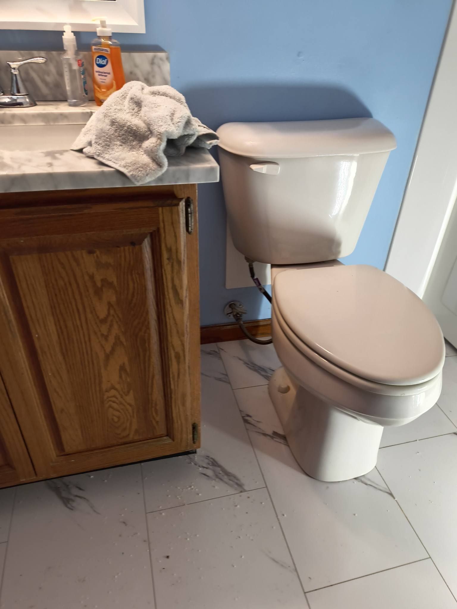Bathroom toilet beside a wooden vanity, with a cloth on the counter and blue wall behind.