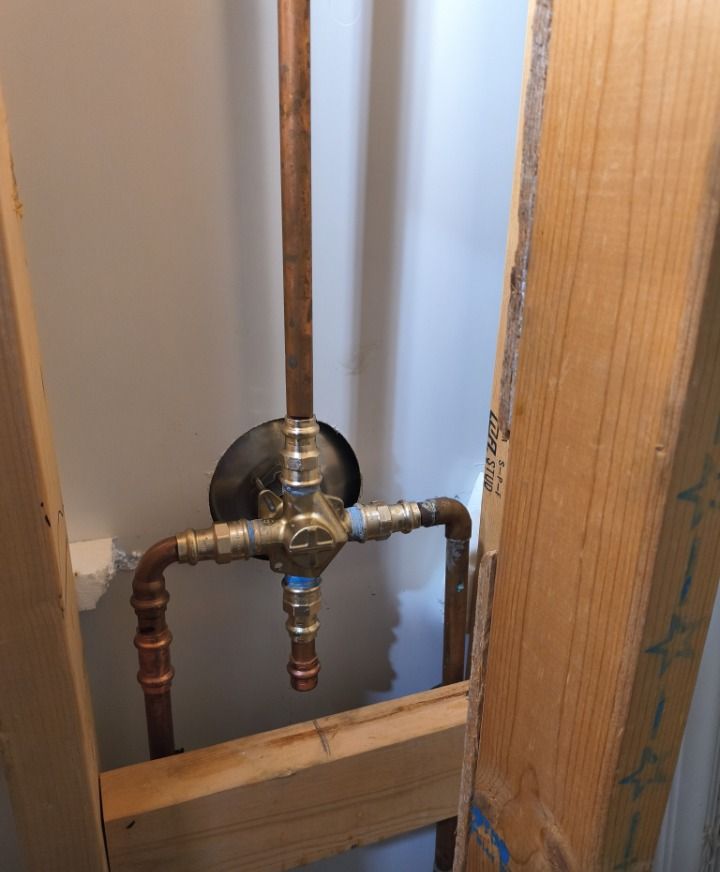 Exposed plumbing valve and pipes inside a wall opening, with wood framing and copper fittings.