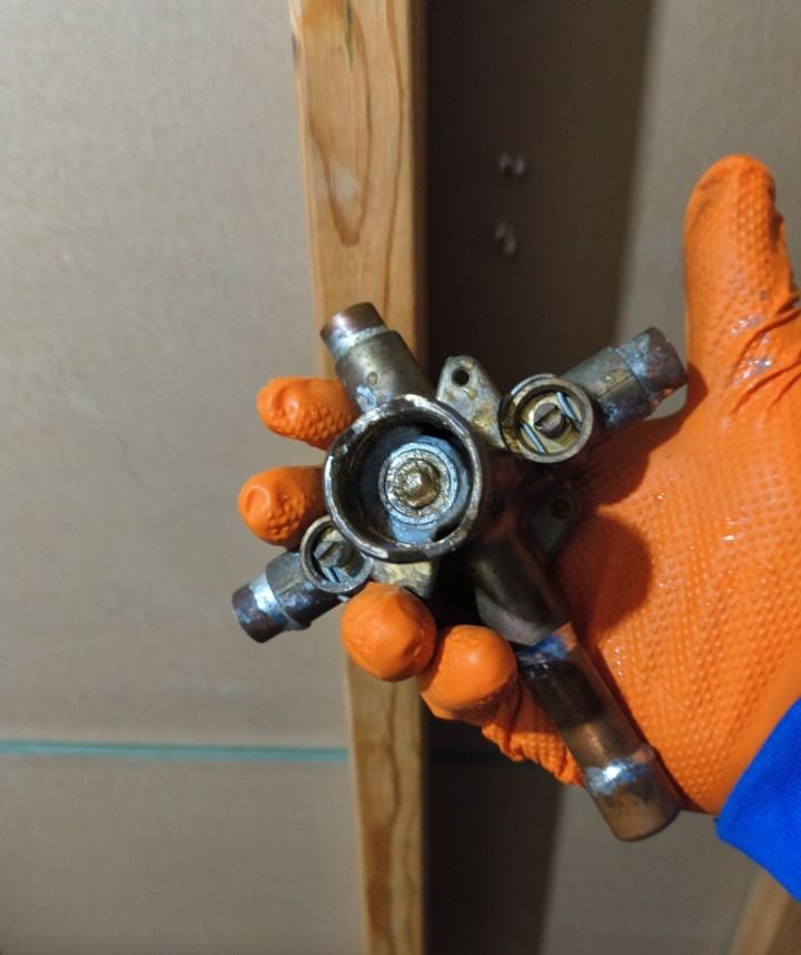 Gloved hand holding a metal plumbing valve assembly with four pipe connectors