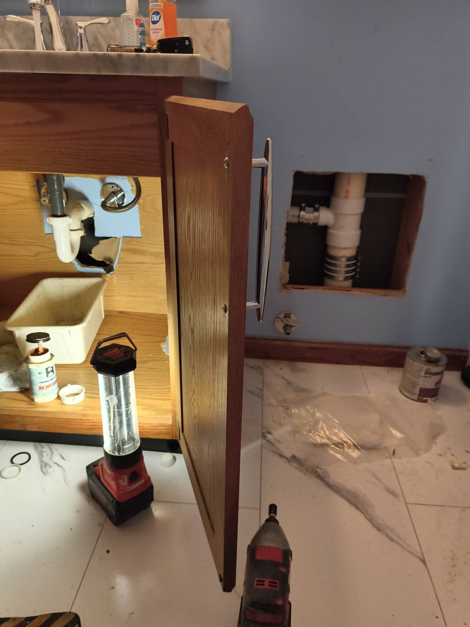 Under-sink cabinet with open door, showing plumbing and tools on a tiled bathroom floor