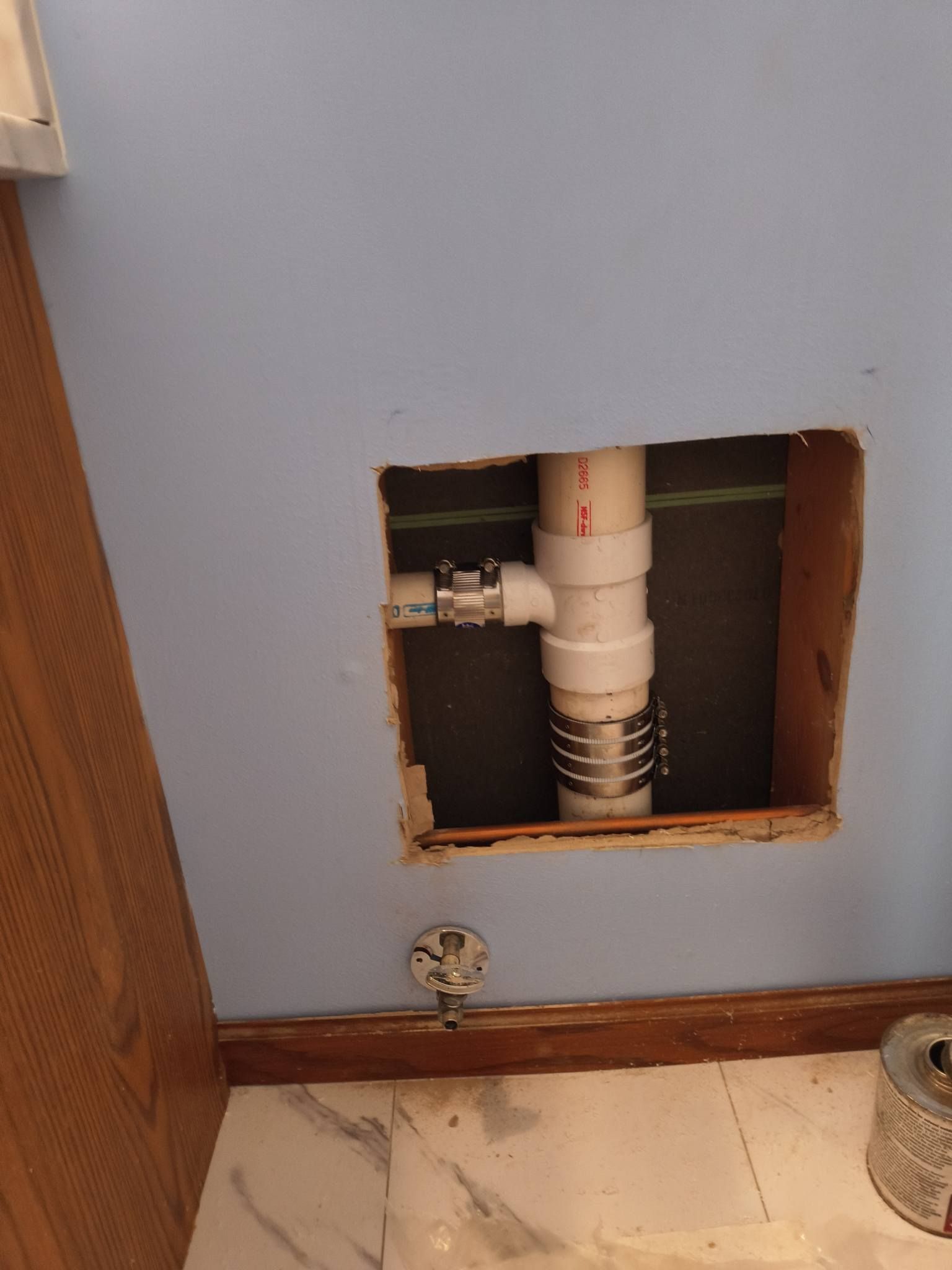 Bathroom wall opening exposing white plumbing pipes beneath a sink.