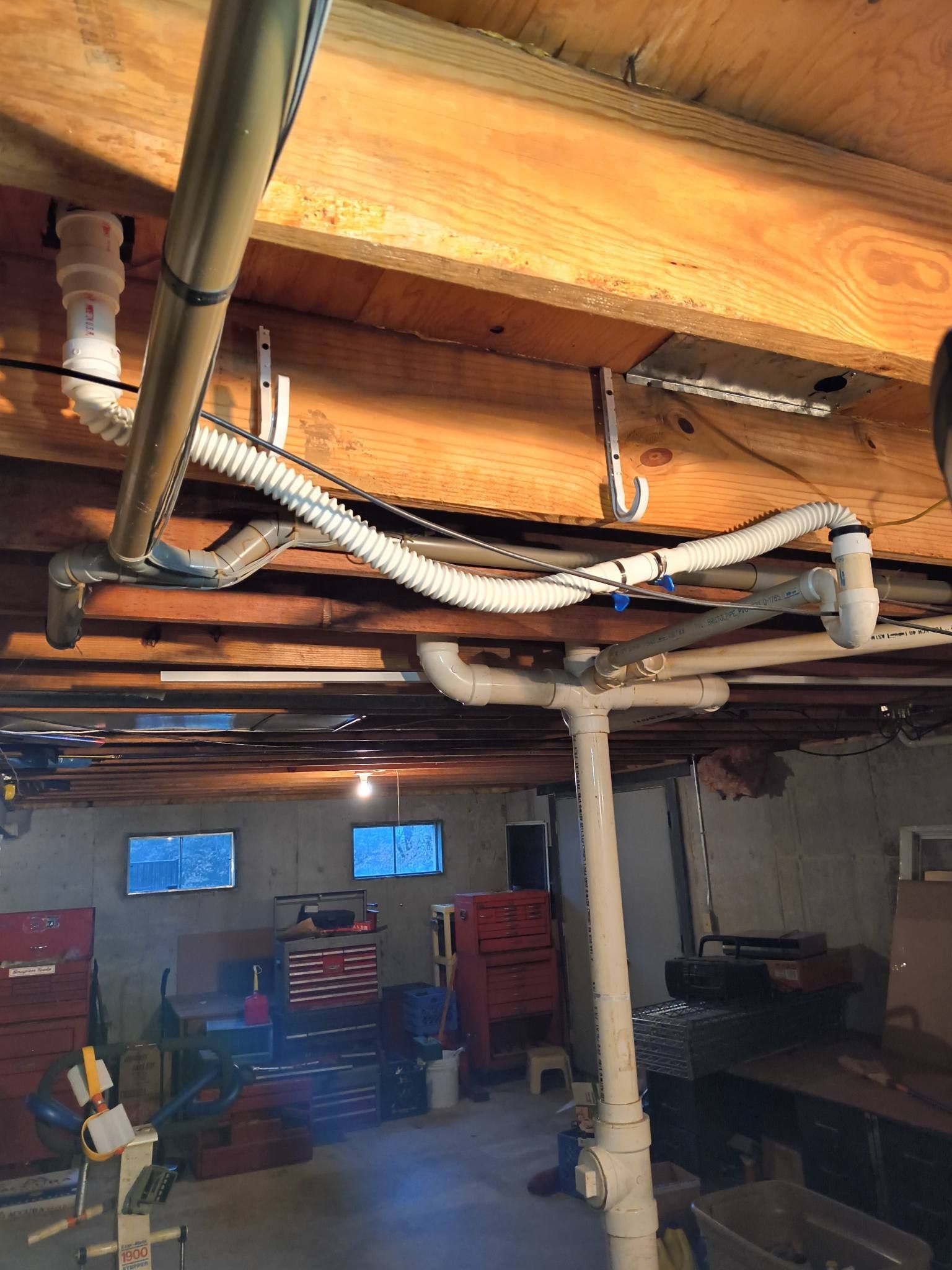 Basement with exposed pipes and beams, laundry area, and storage shelves under a low ceiling