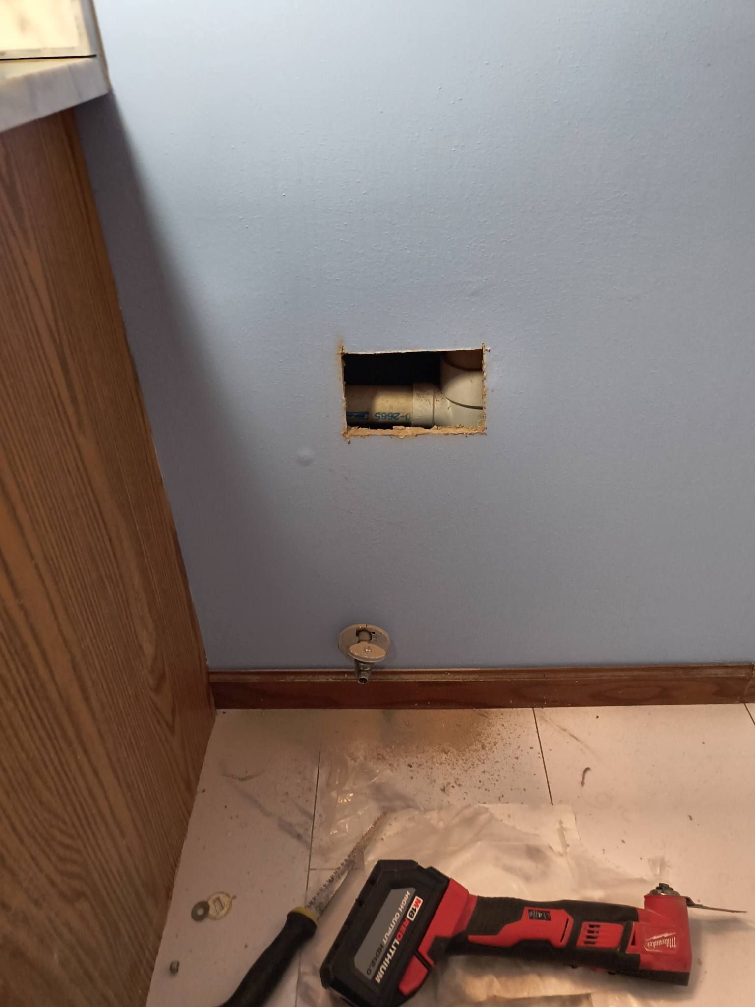 Wall with a rectangular cutout above the baseboard; a red-and-black power drill and dust on the floor.