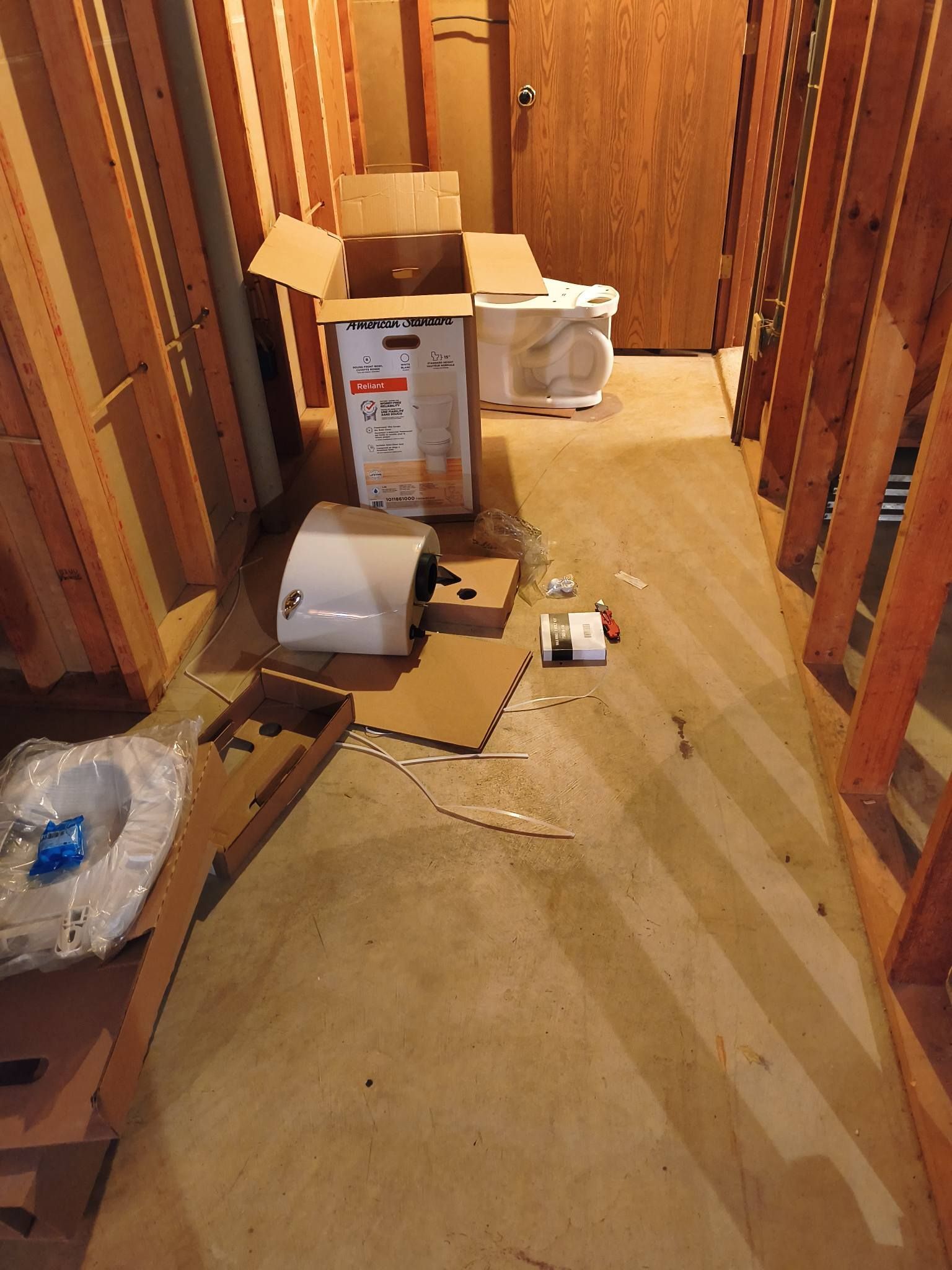 Cluttered hallway with boxes, a fan, and scattered items on the floor in a wooden interior.