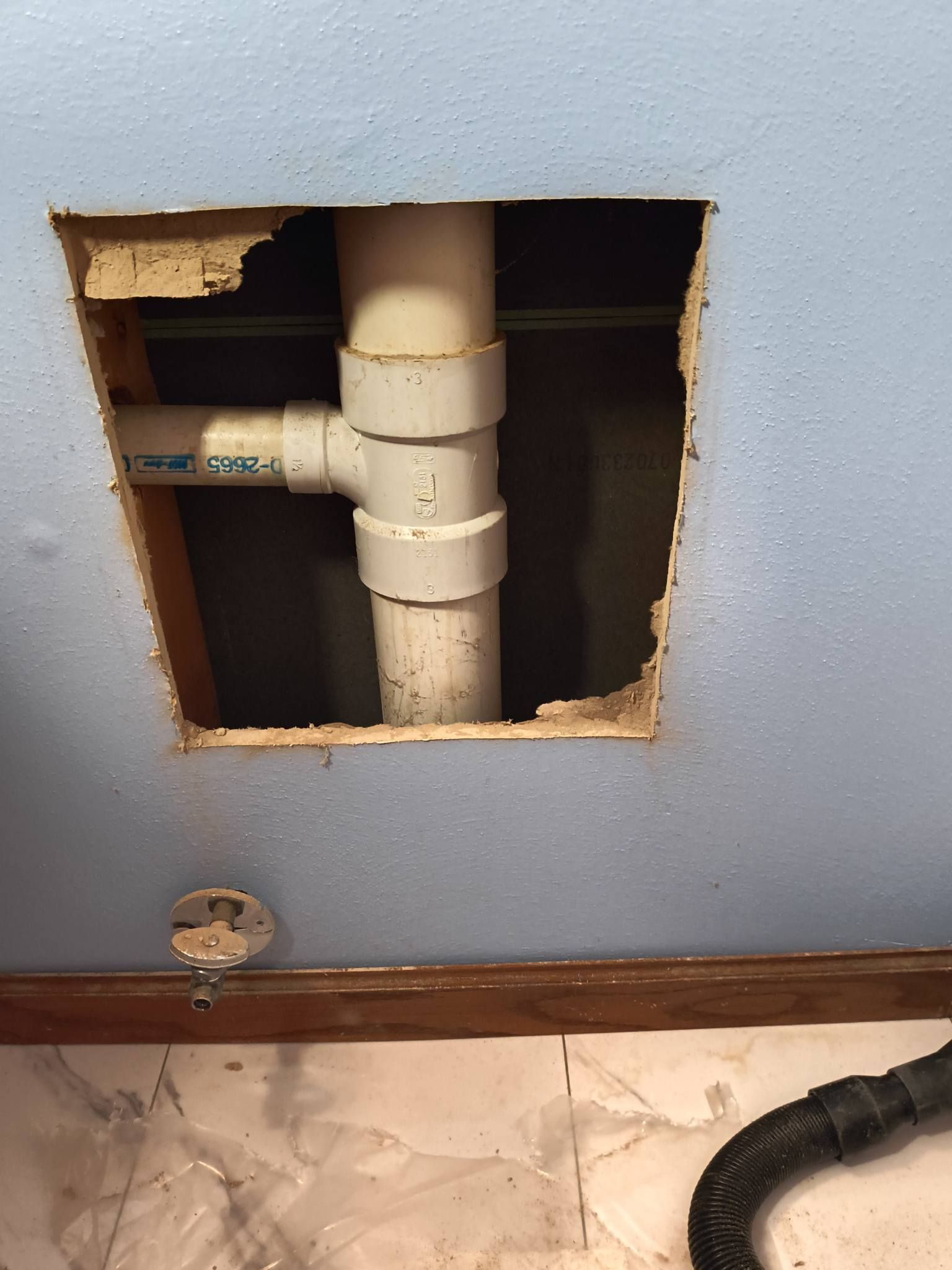 Open wall access to white PVC plumbing pipes above a tiled floor