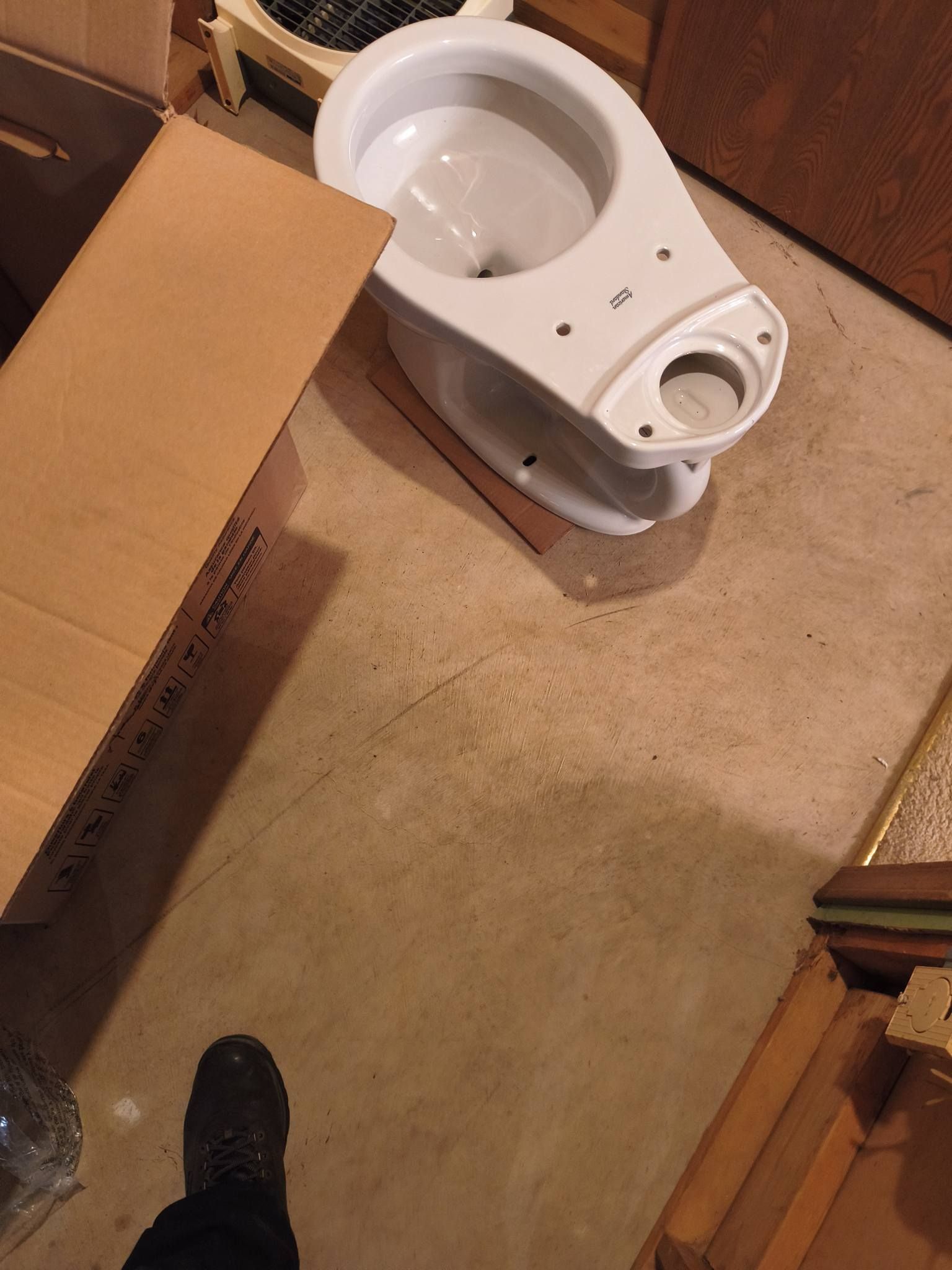 Bathroom under renovation with a white toilet on the floor beside cardboard boxes and a shoe visible in the corner