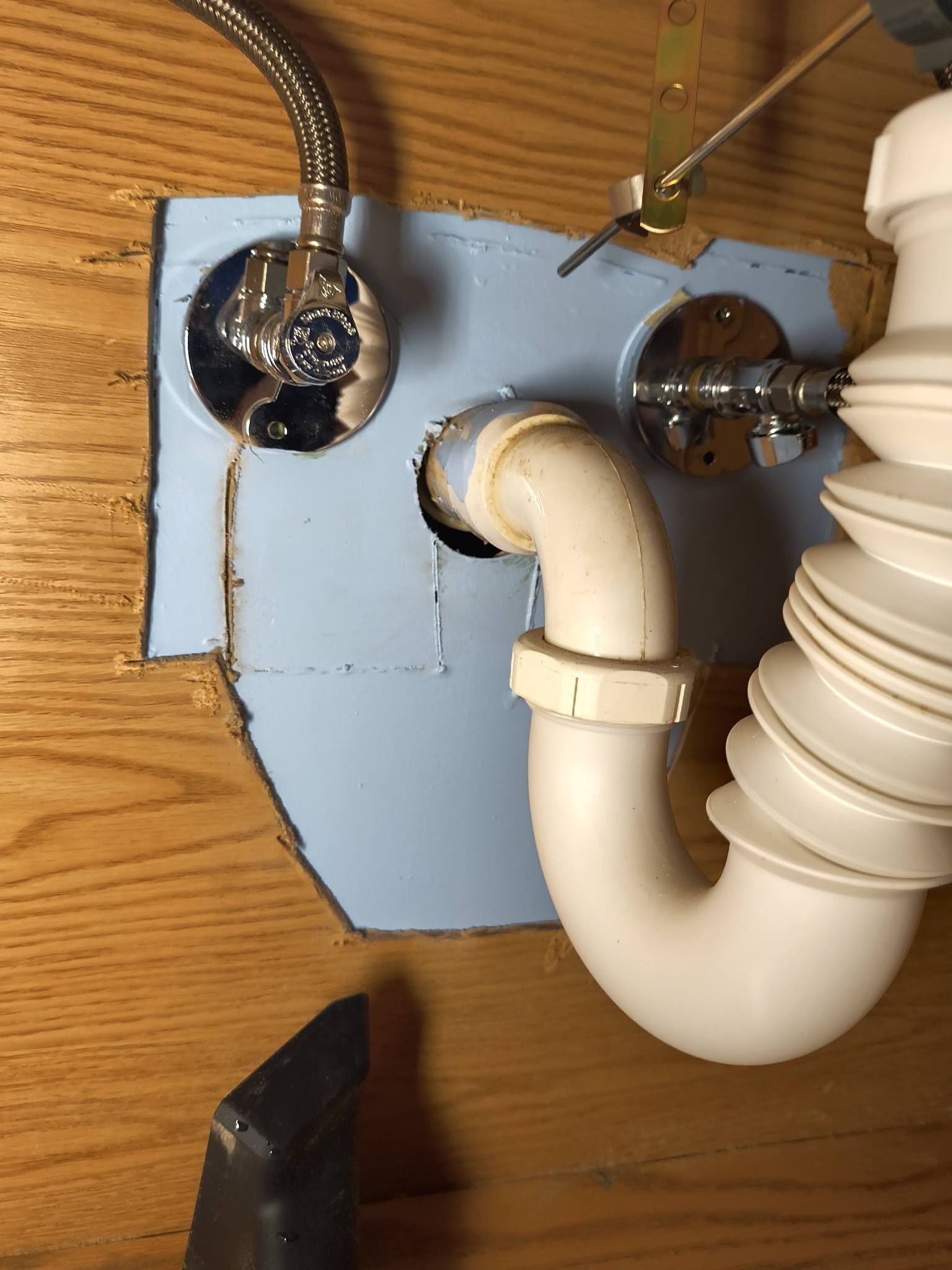 Under-sink plumbing with white drain pipes and chrome faucet connections against a blue mounting plate
