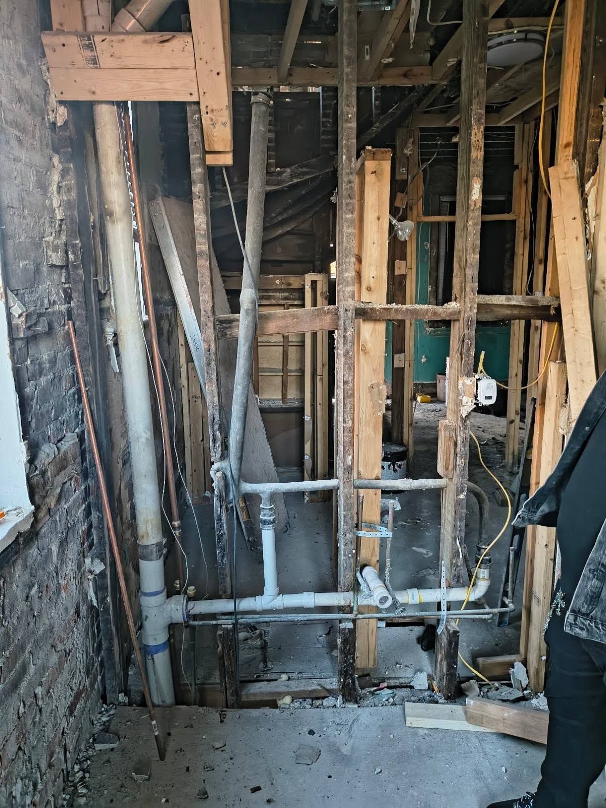 Exposed wall framing and plumbing in a narrow renovation area with old plaster and debris on the floor