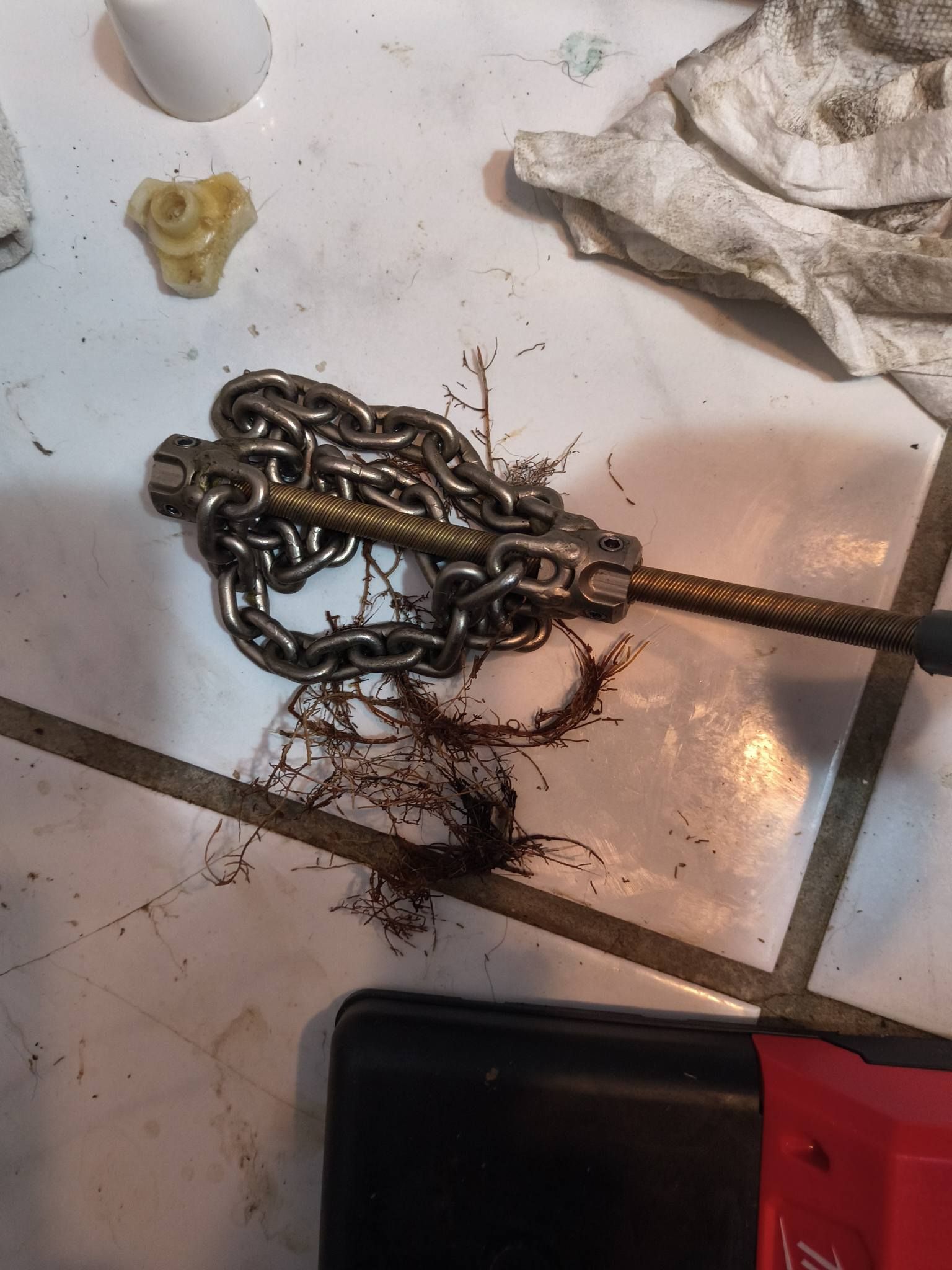 Coiled metal chain on a dirty white floor with rust stains and a red tool in the corner