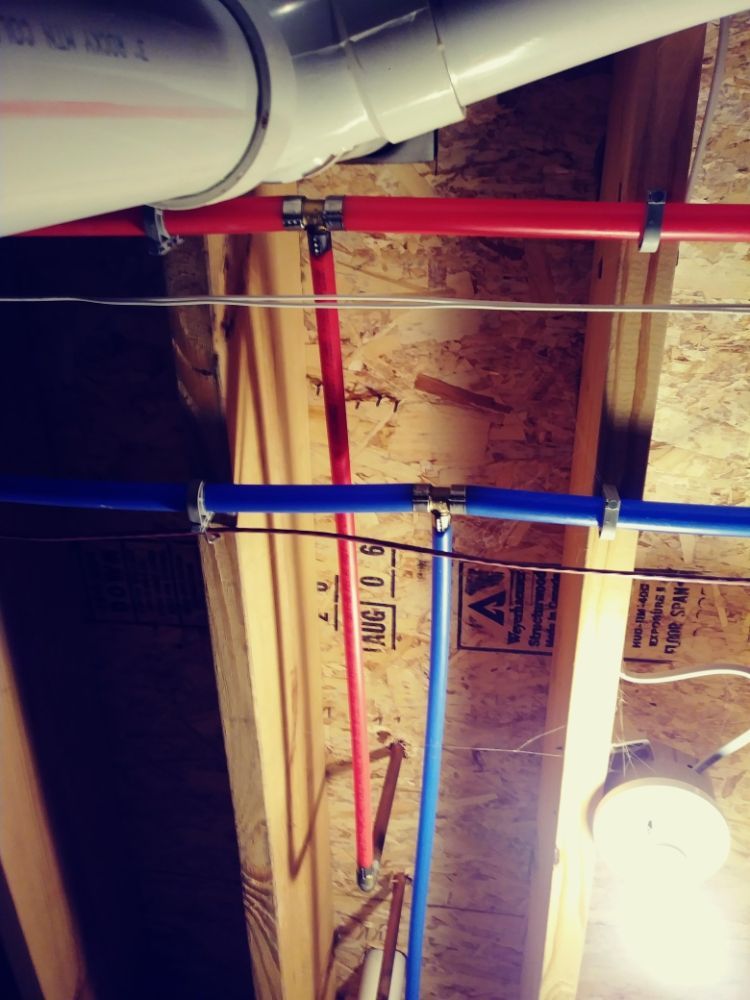 Exposed ceiling with white ductwork, red and blue pipes, and a hanging light in a construction area