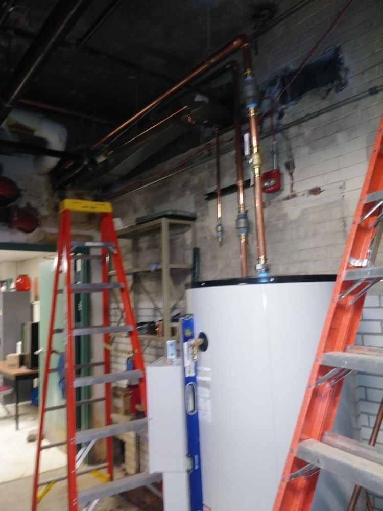 Ladders around a water heater and exposed pipes in a utility room