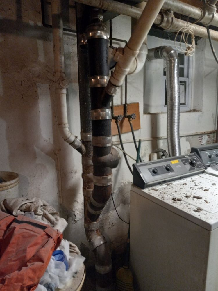 Basement utility area with exposed pipes, a laundry machine, and storage boxes on the floor.