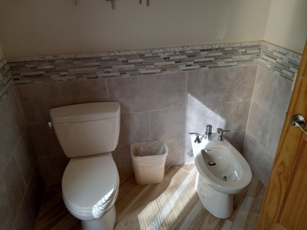 Small bathroom with toilet, trash bin, and bidet against tiled walls.