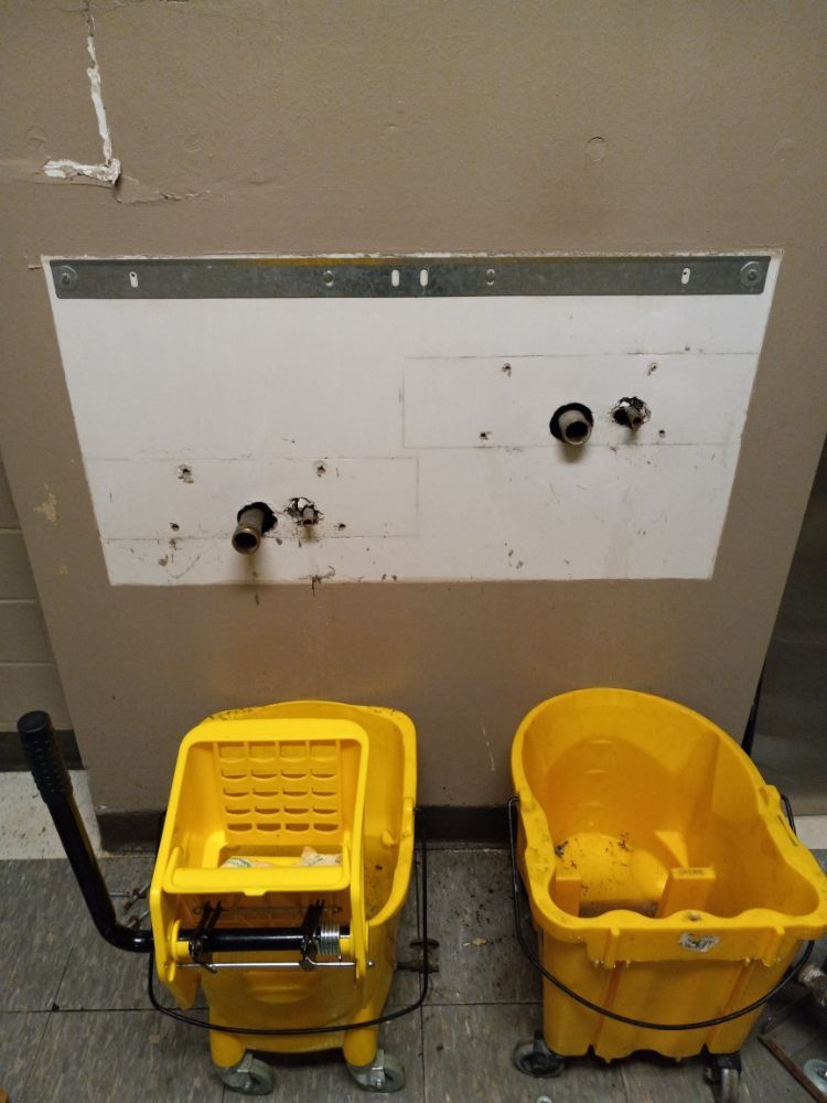 Two yellow mop buckets below a wall-mounted utility sink in a utility room.