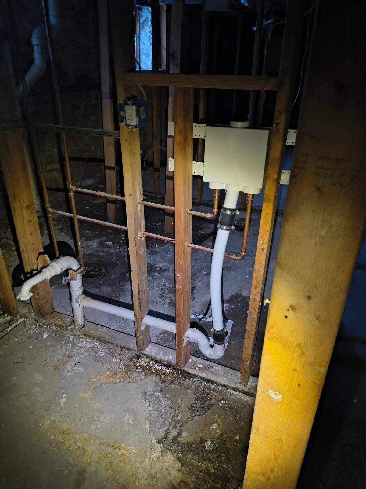 Open wall with exposed plumbing and pipes in a dim unfinished basement