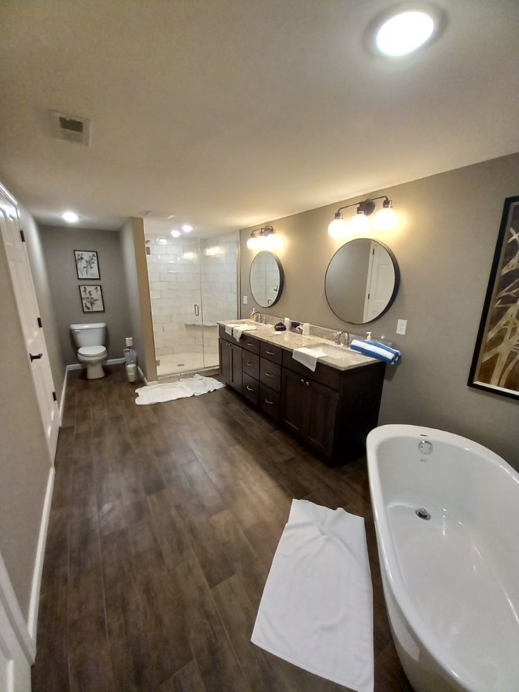 Modern bathroom with bathtub, double vanity, toilet, and wood-look flooring