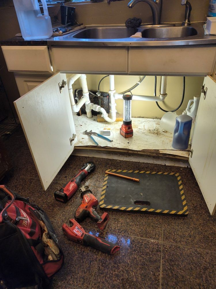 Under-sink cabinet with tools and open access panel, suggesting plumbing repair work