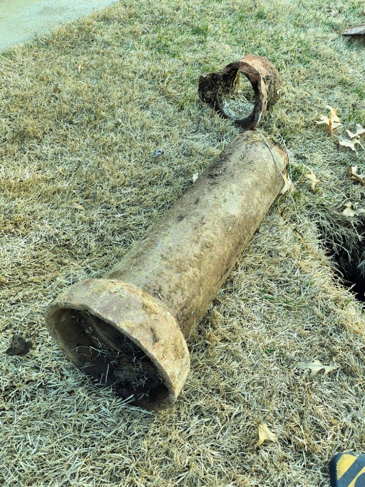 Large rusted metal pipe lying on grass, with a looped strap attached to one end.