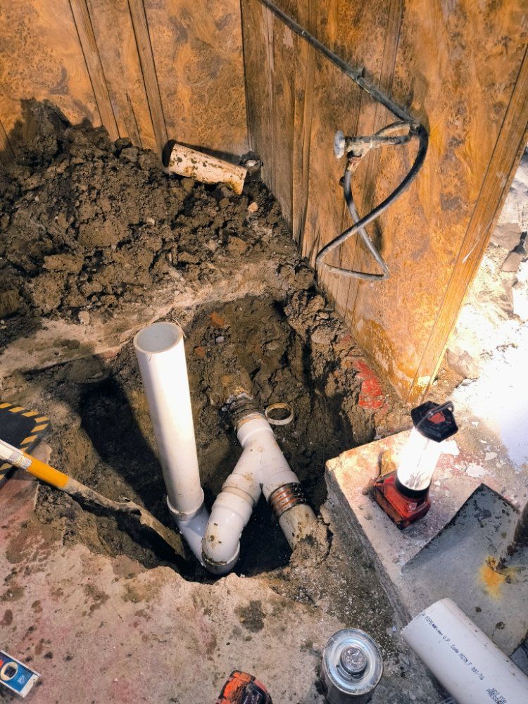 Plumbing rough-in in a dirt-floored basement with white PVC pipes and a red flashlight on a concrete step
