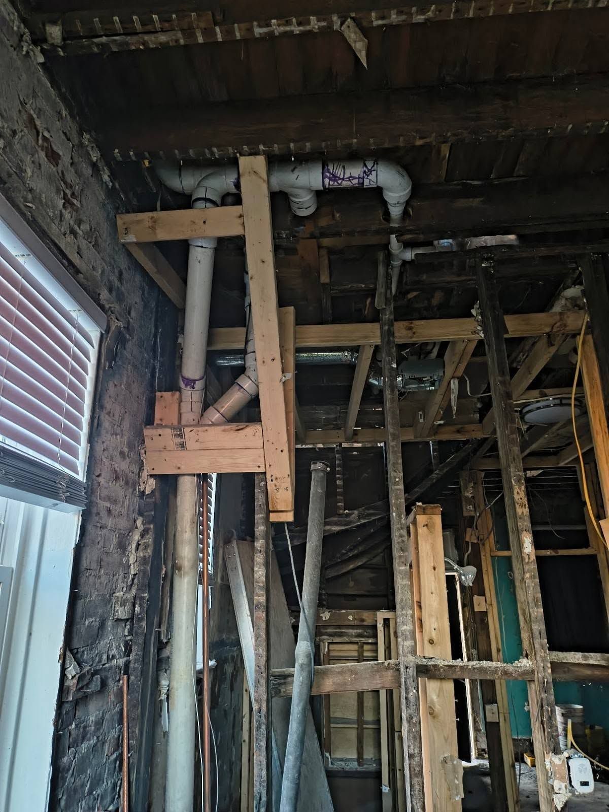 Partially demolished room with exposed wooden studs, beams, and damaged walls under a dark ceiling