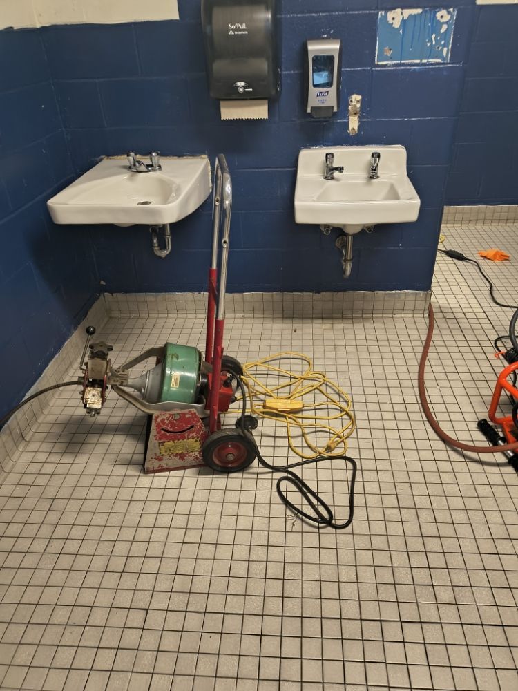 Public restroom with two sinks, cleaning equipment, and cords on a tiled floor