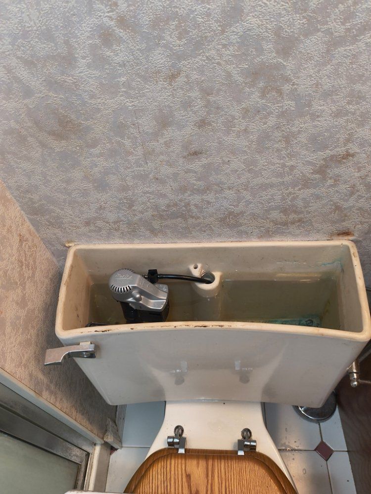 Damaged toilet tank with exposed interior parts and standing water in a small bathroom