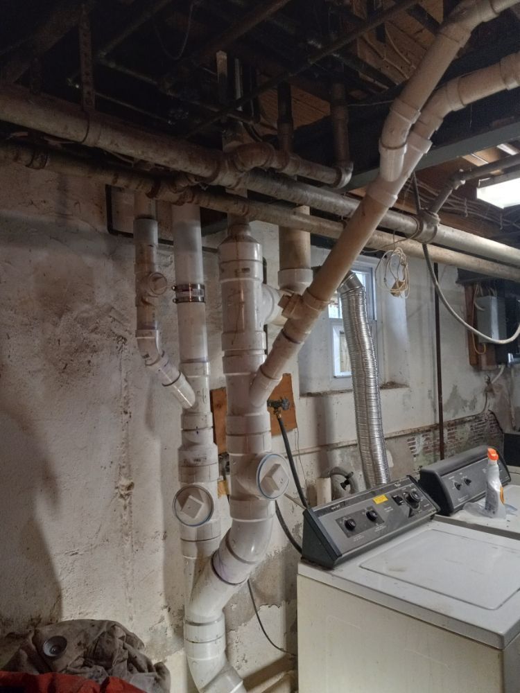 Laundry room with exposed pipes and ductwork above washing machines in a basement.