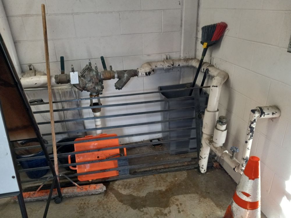Stored equipment and pipes in a basement corner with an orange traffic cone and metal rack.