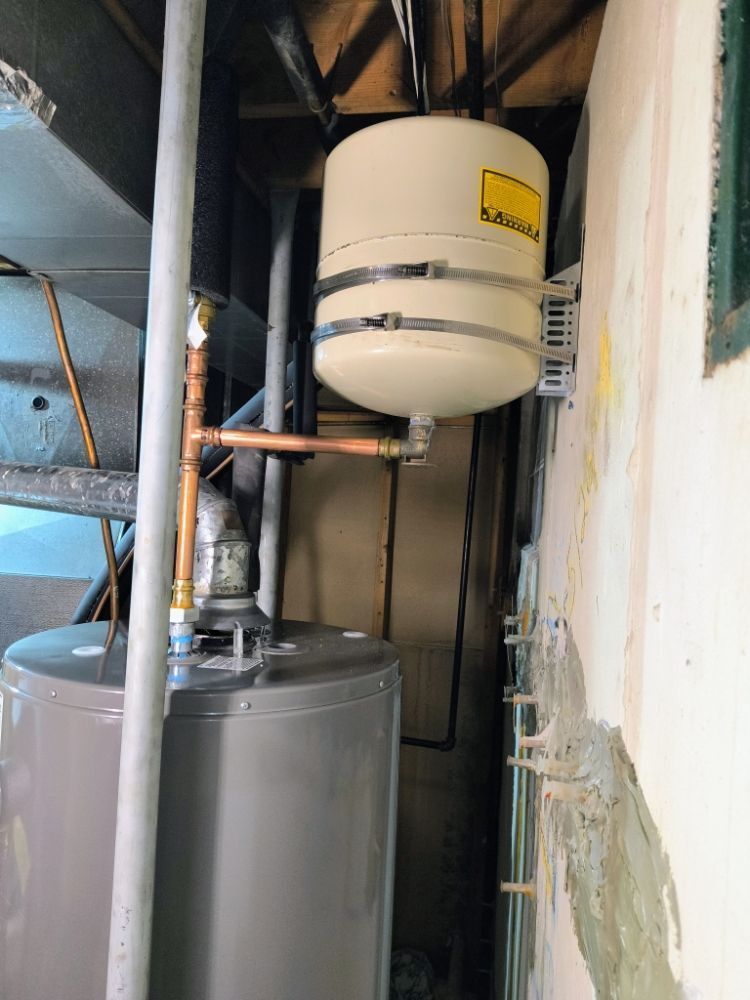 Utility room with gray water tank, white expansion tank, and exposed pipes against a wall
