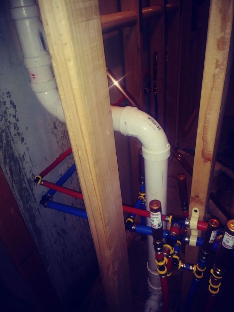 Open wall framing with white plumbing pipes and blue/red water valves in a construction area