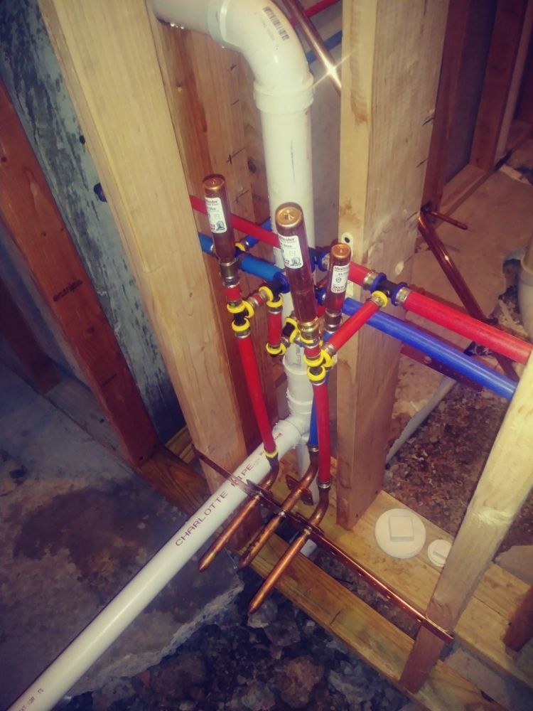 Plumbing manifold with red and blue pipes and yellow valves inside an unfinished wall