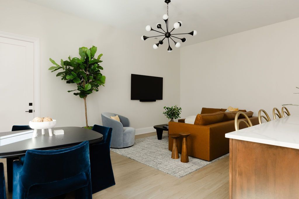 Living room with mustard-colored sofa, blue chairs, black dining table, and large leafy plant.Purple Martin Hotel