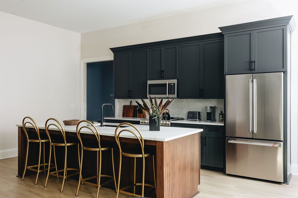 Kitchen with dark blue cabinets, stainless steel refrigerator, island with gold stools, and wood floor. Purple Martin Hotel