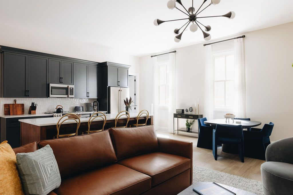 Modern living room with kitchen island, dark cabinets, leather sofa, and dining area.
