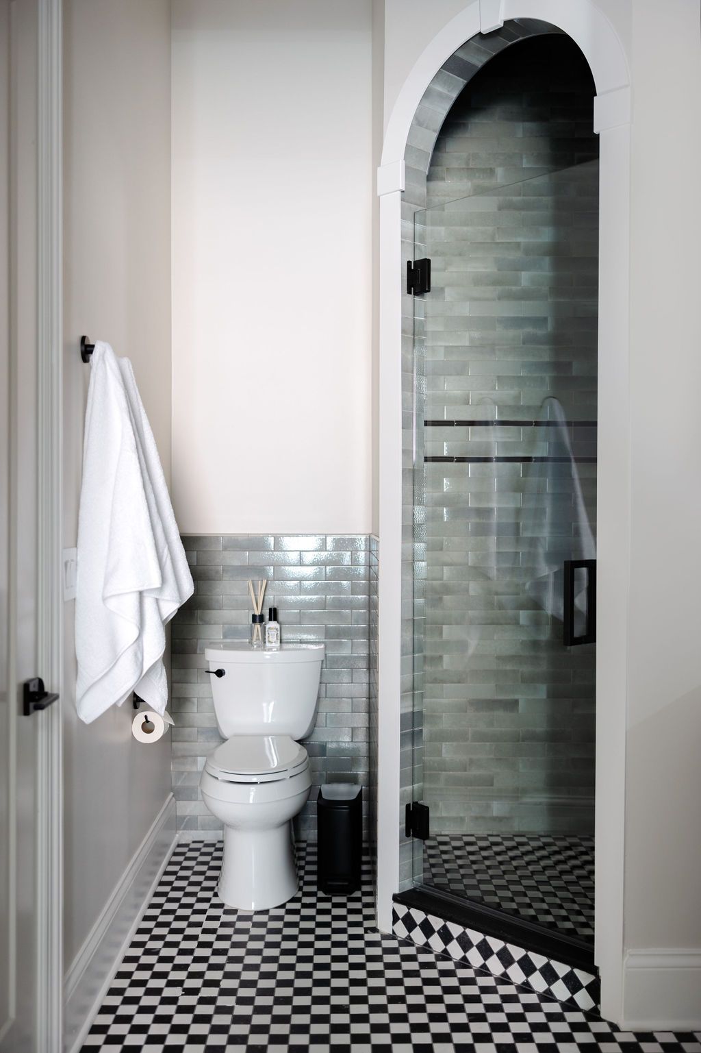 Bathroom with black and white checkered floor, toilet, and glass shower with blue-green tile.