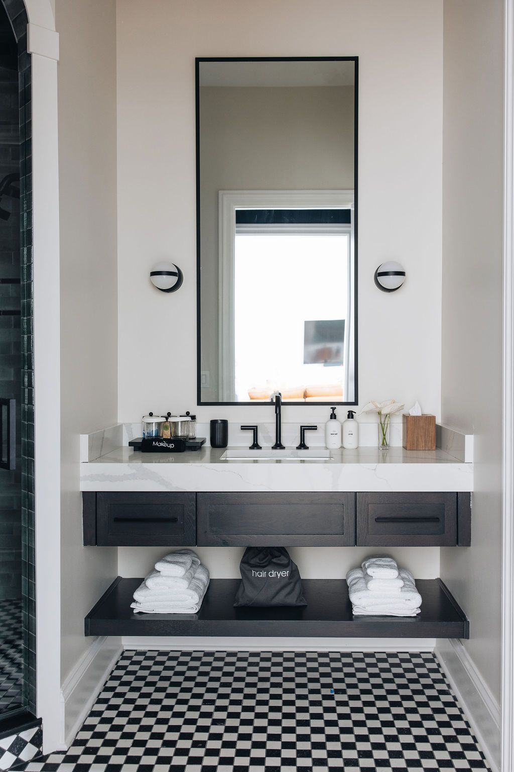 Bathroom with black and white checkered floor, floating dark vanity with mirror, and white countertop.