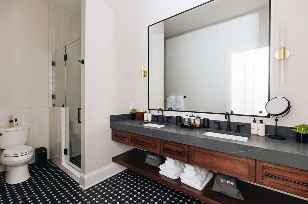 Bathroom with a black and white tiled floor, floating wood vanity, large mirror, and glass shower. Purple Martin Hotel