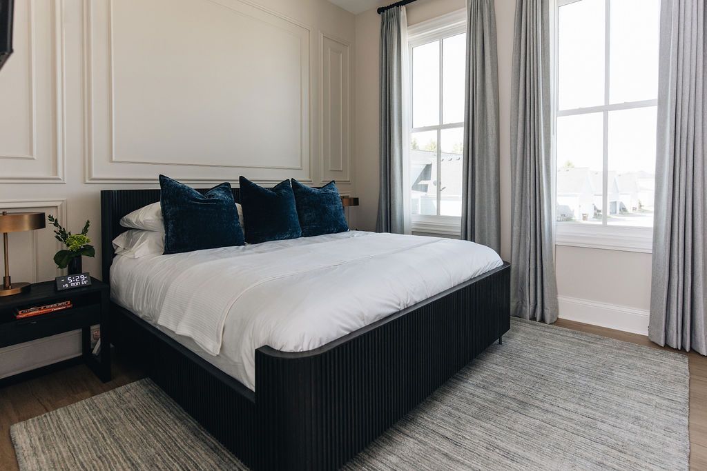 Bedroom with black bed, white bedding, blue pillows, gray curtains, and rug. Purple Martin Hotel